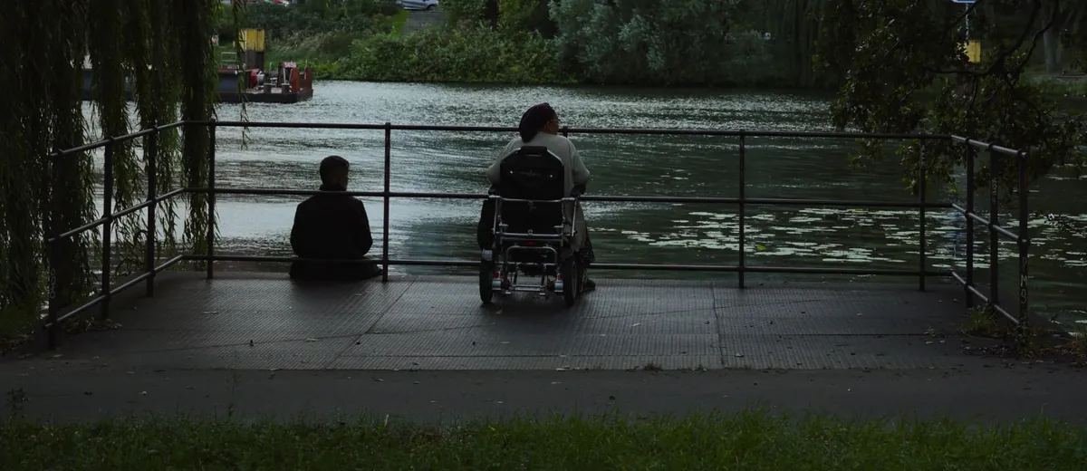 Člověk na invalidním vozíku odpočívá u řeky v parku