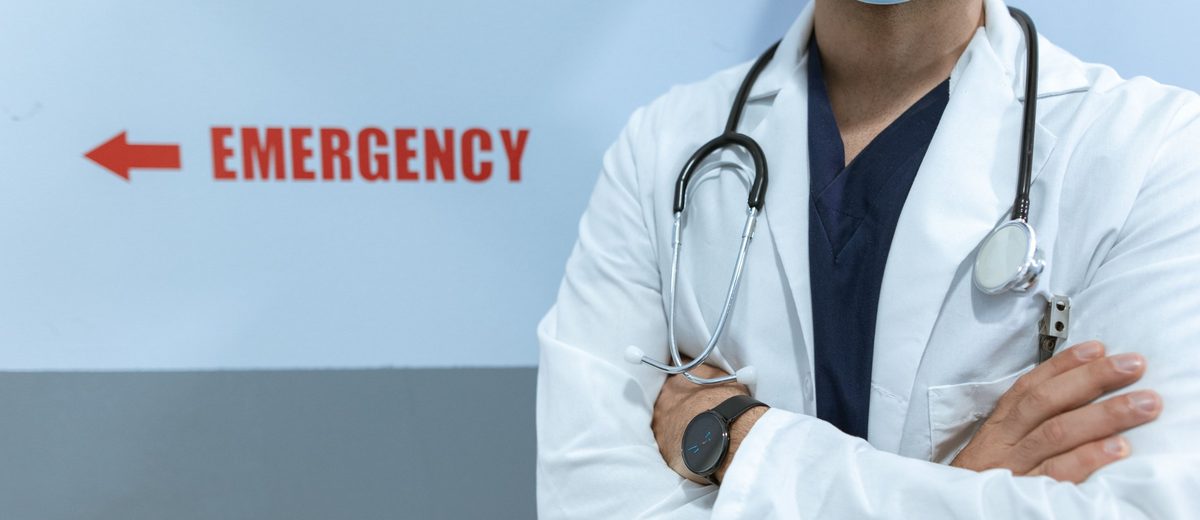 Lékař se stetoskopem stojí u nápisu Emergency