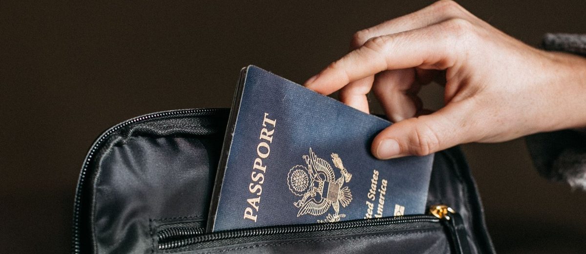 Ruka vkládá cestovní pas do cestovní tašky