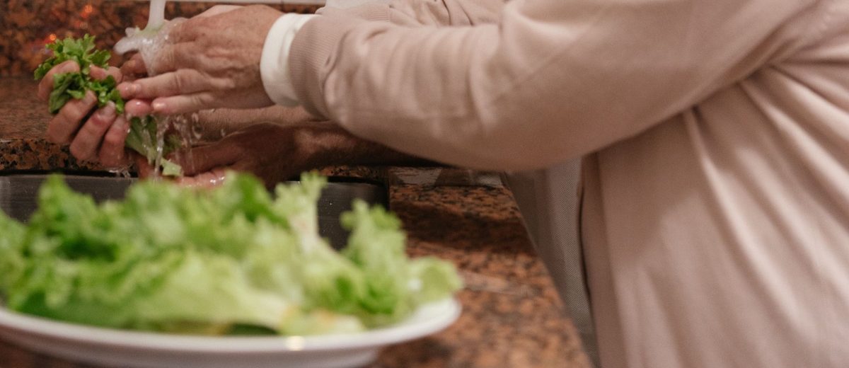 Ruce pečovatelky a seniora při přípravě salátu v kuchyni