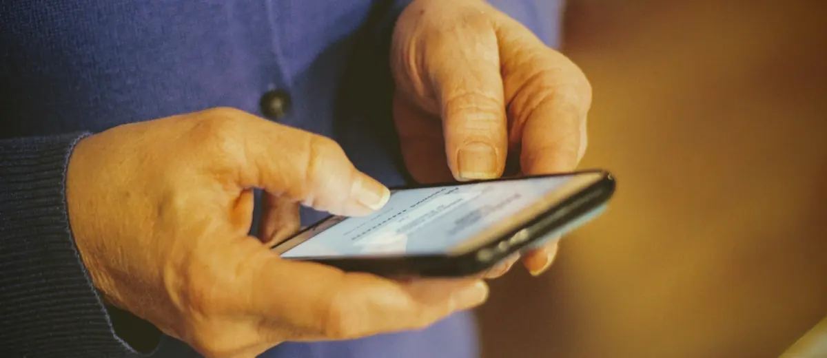 Ruce seniorky držící mobilní telefon s otevřenou zprávou