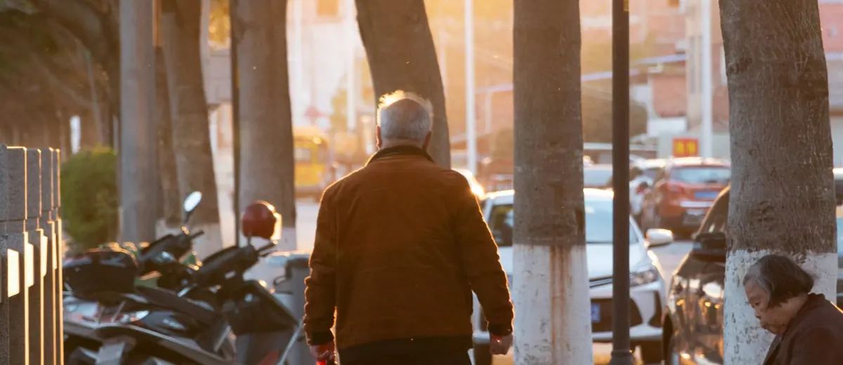 Senior s taškou jde po chodníku ve městě