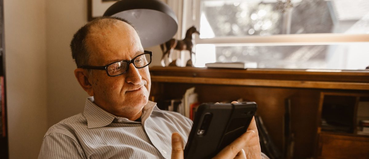 Senior s brýlemi drží doma mobilní telefon a volá