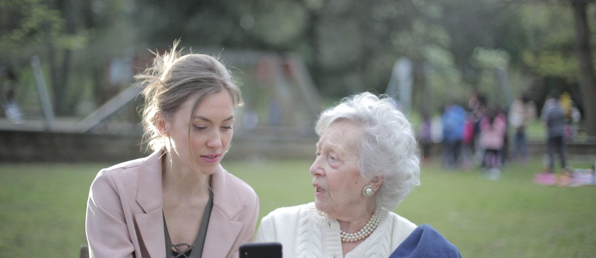 Seniorka s mladší ženou sedí na lavičce v parku